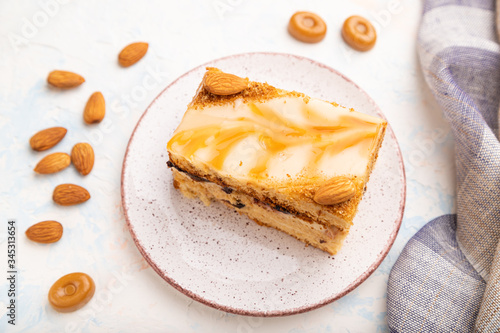 Honey cake with milk cream, caramel, almonds and a cup of coffee on a white concrete background. Side view, selective focus.