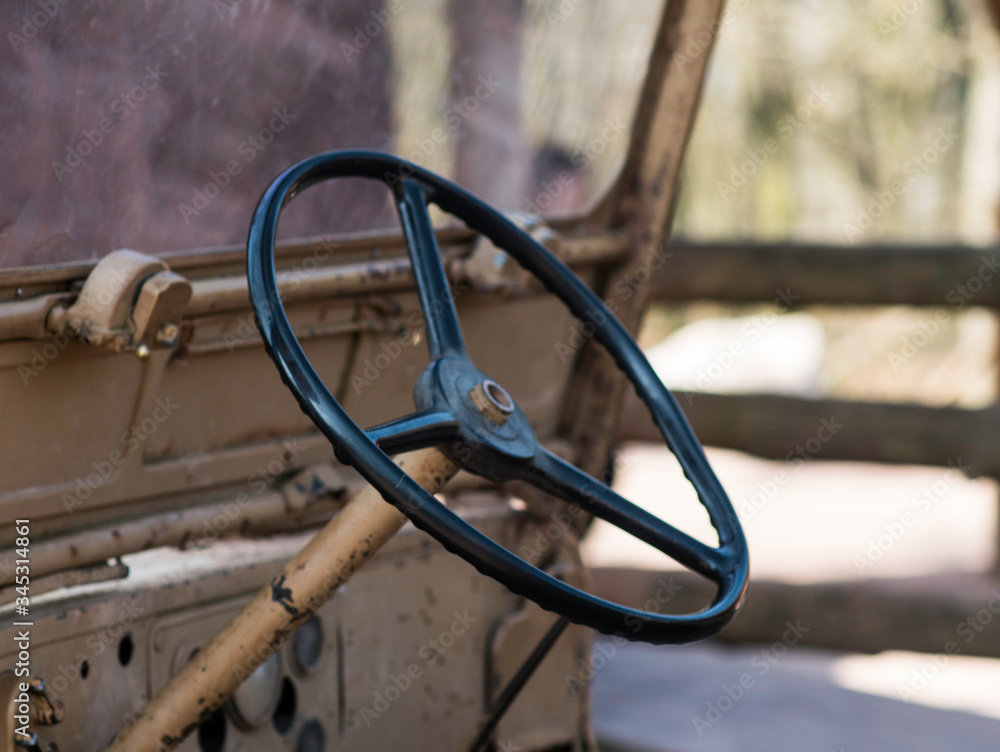 Detail of the steering wheel of an old stationary jeep. Rusty parts of the front dashboard.