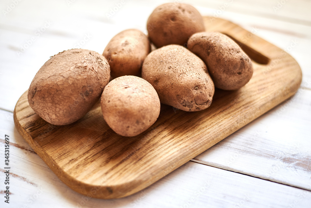 Raw potato tubers on a wooden background.