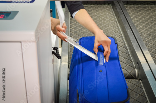 Check-in employee attaches a luggage tag to suitcase of passenger - closeup of hands