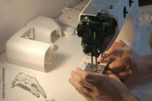 Repairman master is repairing sewing machine on table, hands closeup. Man is testing and disassembles the sewing machine in workshop. Maintenance and repair of home appliances. photo