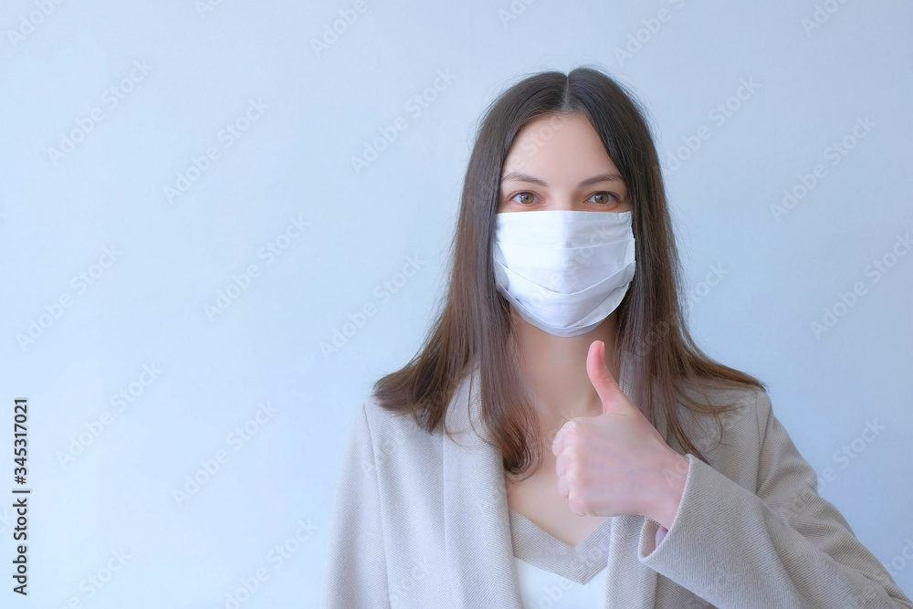 Portrait woman in mask in coronavirus pandemic with thumb up on white bakground. Girl in protective medical mask wearing in suit. COVID-19 pandemic, epidemic, quarantine. Protection of health.
