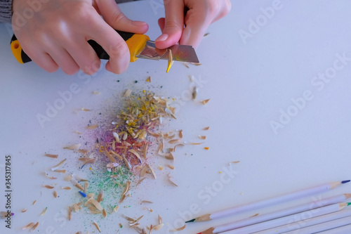 Woman painter artist sharpening yellow pencil using sharp knife, hands closeup. Teacher sharpen blue pencil for her students on white table. Preparing to work in art studio. photo