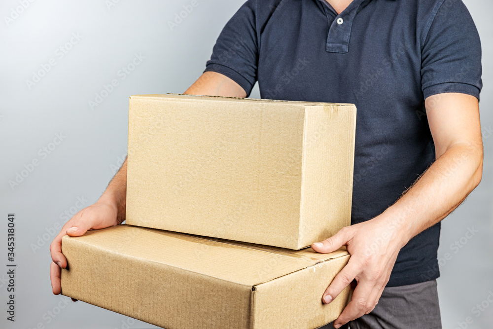 Delivery service by courier with parcels in hand on a light gray background, shallow depth of field, selective focus. Delivery service by courier with parcels in hand on a light gray background, shallow depth of field, selective focus.