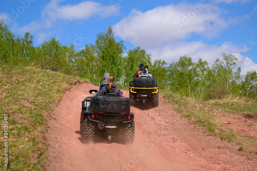 Young people with girls ride ATVs. Mountainous terrain. Dusty road is red. View from the back. Concept of adventure, tourism.