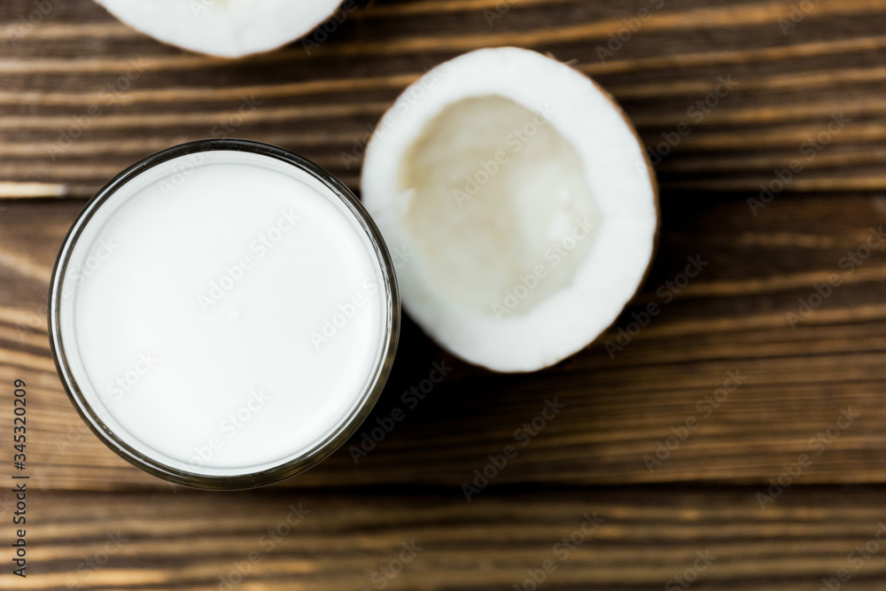 Coconut vegan milk in a glass and coconut broken in half on a dark wooden background Coconut vegan milk in a glass and coconut broken in half on a dark wooden background