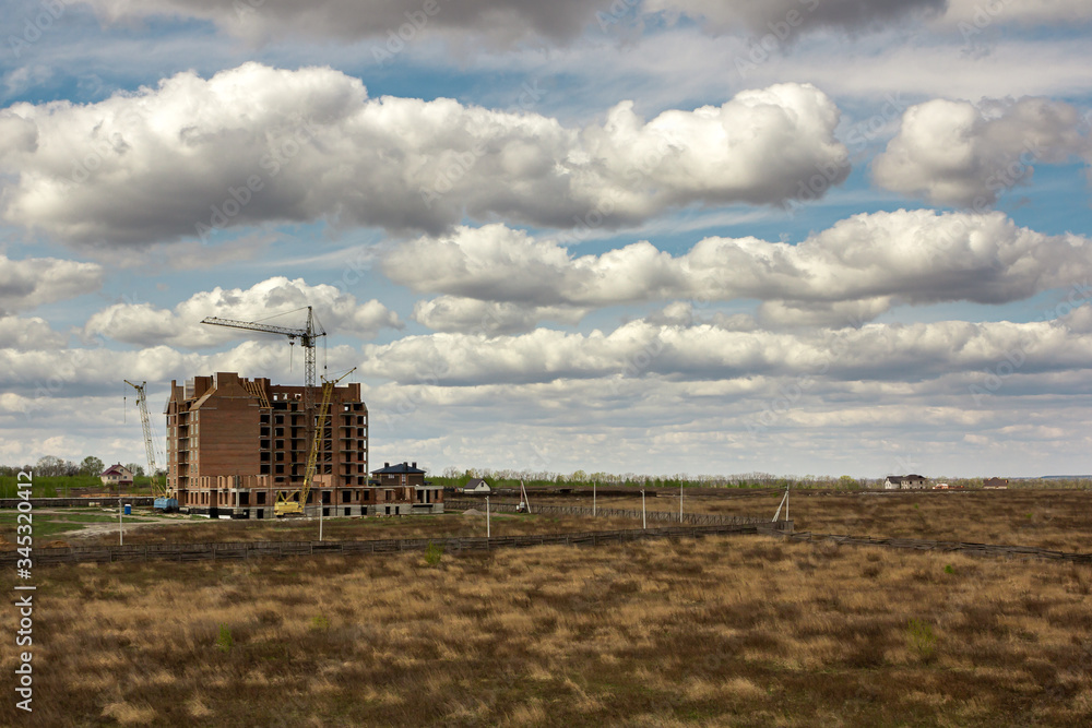 Beautiful blue sky with white cumulus clouds above spring field. Construction new building. Cloudscape background.