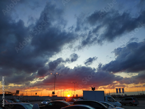 Beautiful sky with clouds and sunset in an open parking lot with silhouettes of cars.Urban urban landscape and nature in all its beauty.Wonderful life in the city, magnificent sunset in yellow and red © Leria Kaleria