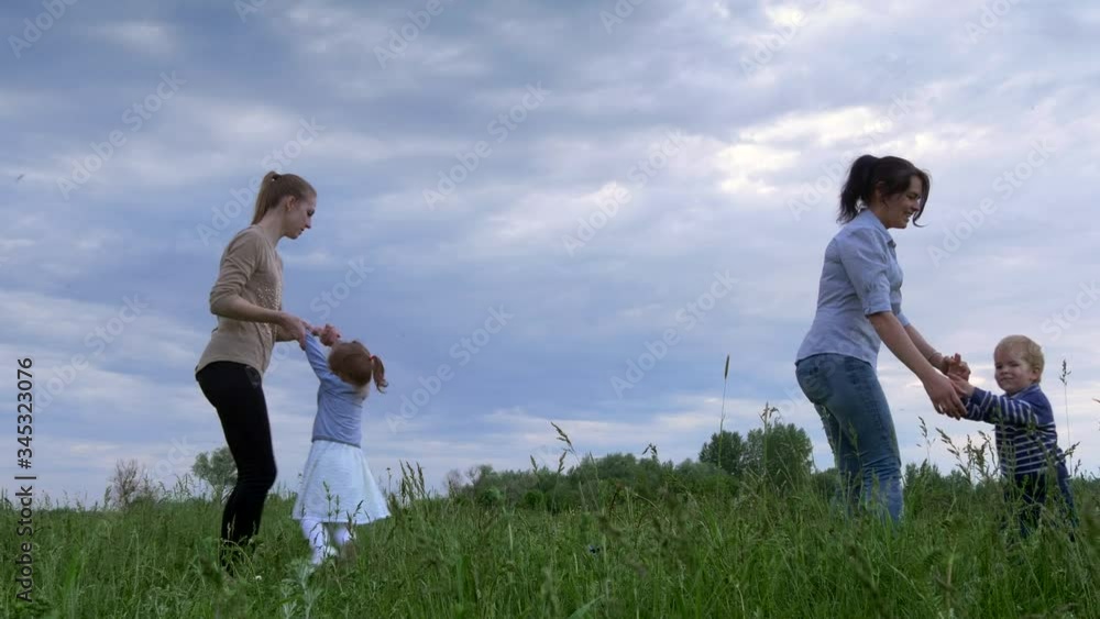 Mothers play with Children on Nature in the Grass Field. Evening Cloudy Sunset Sky