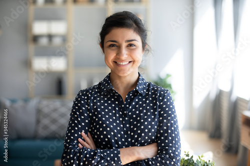 Head shot portrait smart confident smiling millennial indian woman standing with folded arms at home. Attractive young hindu teenager student girl freelancer looking at camera, posing for photo. photo