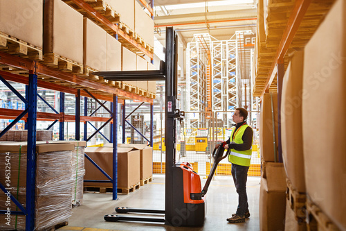 Storehouse employee in uniform working on forklift in modern automatic warehouse. Boxes are on the shelves of the warehouse. Warehousing, machinery concept. Logistics in stock. photo