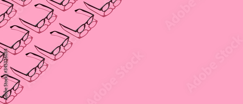 Many black hipster eyeglasses on pastel pink abstract background border frame. Fashionable eyewear concept. photo