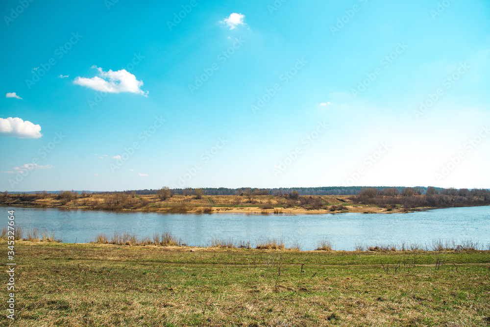 Spring landscape with blue sky, river and meadow