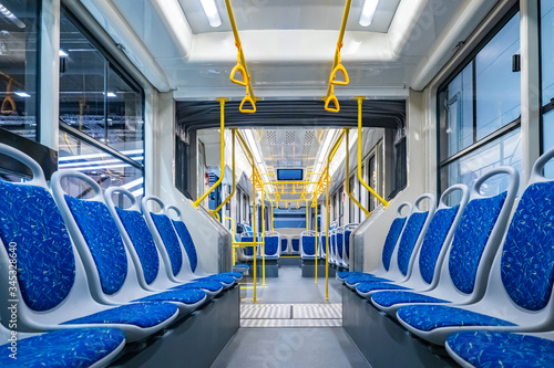 Public transport. Empty interior of the city bus. Rows of blue passenger seats and yellow handrails. The interior is equipped with handrails and hanging handles.