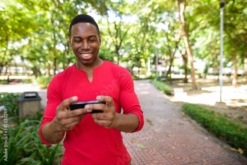 Happy young handsome African man using phone at the park