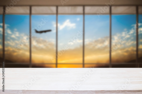 Empty wooden desk space and blurry background of airport for product display montage.
