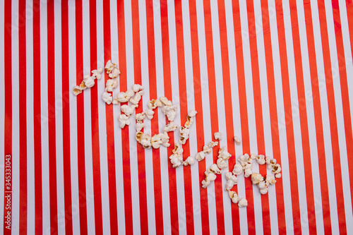 Popcorn grains arranged in movie word on red white striped background. Concept of watching movie tv cinema.