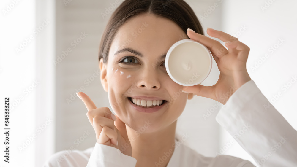 Portrait of excited millennial Caucasian female apply nourishing facial cream or under eye beauty product, smiling young woman recommend moisturizing face mask for healthy skin, skincare concept Portrait of excited millennial Caucasian female apply nourishing facial cream or under eye beauty product, smiling young woman recommend moisturizing face mask for healthy skin, skincare concept