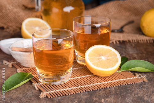 A glass of iced tea with mint and lemon on a wooden table.A glass cup of tea with lemon, mint, and honey on a wooden rustic table.