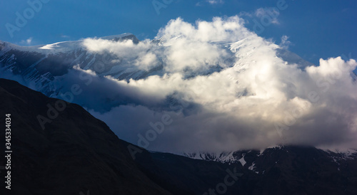 Sunlight hitting the clouds swarming around the snow covered peak of Mount Tukuche on the Annapurna circuit in Nepal.