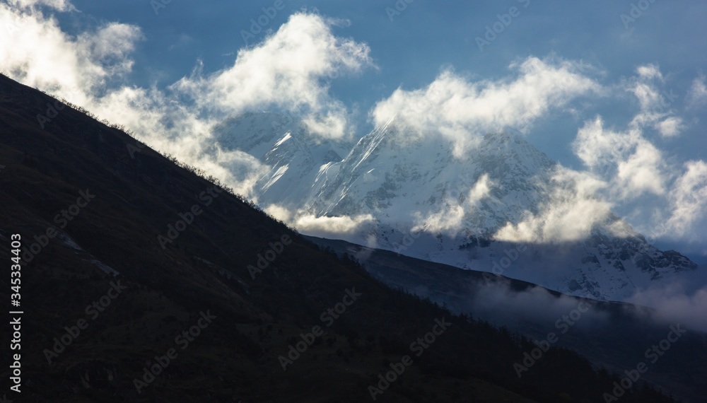 Sunlight hitting the clouds and slanting across the snow covered peak of Mount Tukuche on the Annapurna circuit in Nepal.