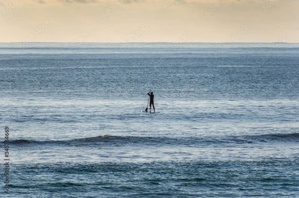 Lone paddle boarder on a calm sea in the afternoon