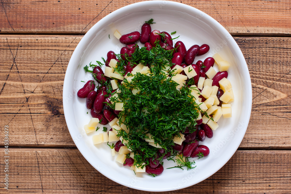 Step-by-step preparation of salad with smoked sausage, cheese, crackers and red beans, step 4 - adding chopped dill, top view, selective focus Step-by-step preparation of salad with smoked sausage, cheese, crackers and red beans, step 4 - adding chopped dill, top view, selective focus
