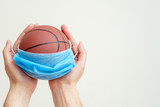 Basketball ball with medical mask in man hands on white background.