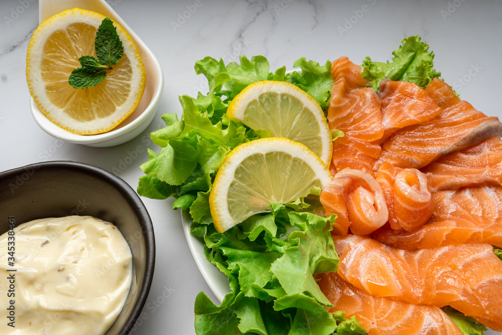 Raw salmon slice or salmon sashimi with green oak salad, lemon and white sauce in Japanese style on white marble background. top view Raw salmon slice or salmon sashimi with green oak salad, lemon and white sauce in Japanese style on white marble background. top view