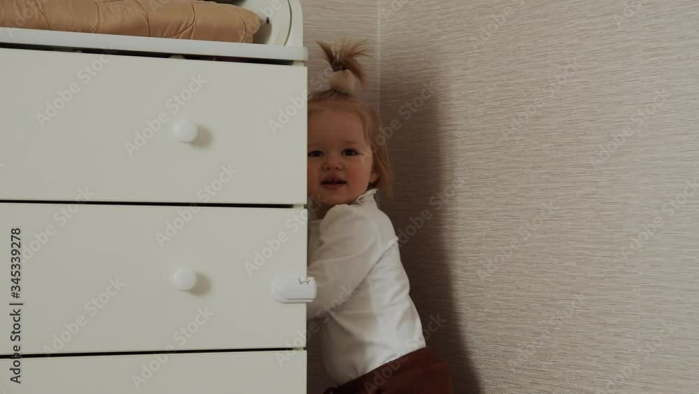 Portrait of cute baby girl playing hide at home. Children funny game.