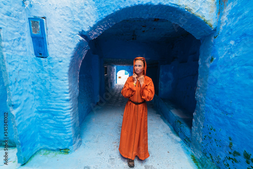 bright orange national clothes on a girl standing in the blue city of Morocco at the entrance to the tunnel © nelen.ru