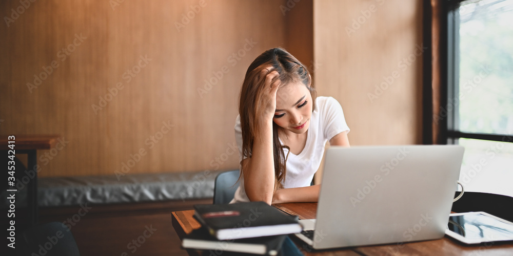 Stressed woman keep hand on head and looking into her computer laptop while suffering a problem from work and sitting at the wooden working desk over orderly living room as background. Stressed woman keep hand on head and looking into her computer laptop while suffering a problem from work and sitting at the wooden working desk over orderly living room as background.