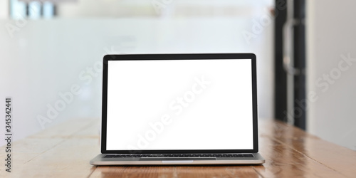 White blank screen computer laptop putting on wooden working desk over comfortable office glass wall as background.