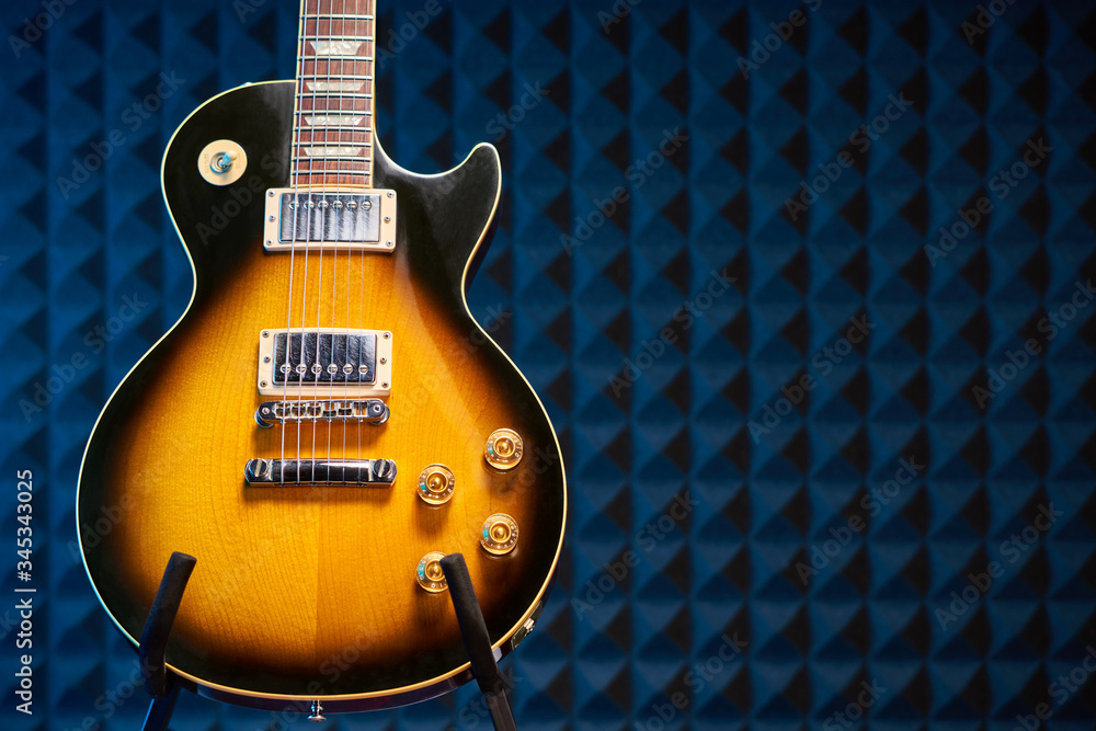 Fototapeta premium Sunburst electric guitar standing over acoustic foam panel background