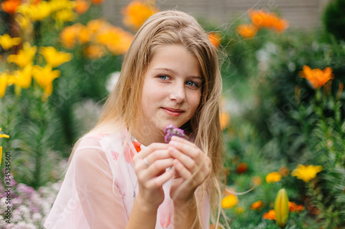 beautiful blue-eyed girl with long blond hair. little girl in a pink flamingo dress. girl in the flower garden. summer bright, emotional photo. large, thick, bright flower garden near the house. 