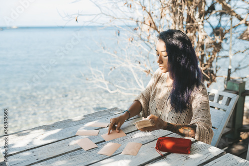 Woman is reading Tarot cards sitting at the table outdoors