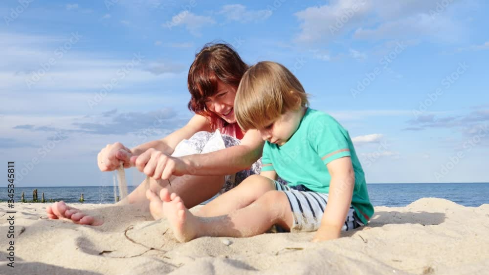 Mother playing with little child boy on sand beach. Adult woman and her son enjoying summer day on seshore. Family holiday at sea. Slow motion Mother playing with little child boy on sand beach. Adult woman and her son enjoying summer day on seshore. Family holiday at sea. Slow motion