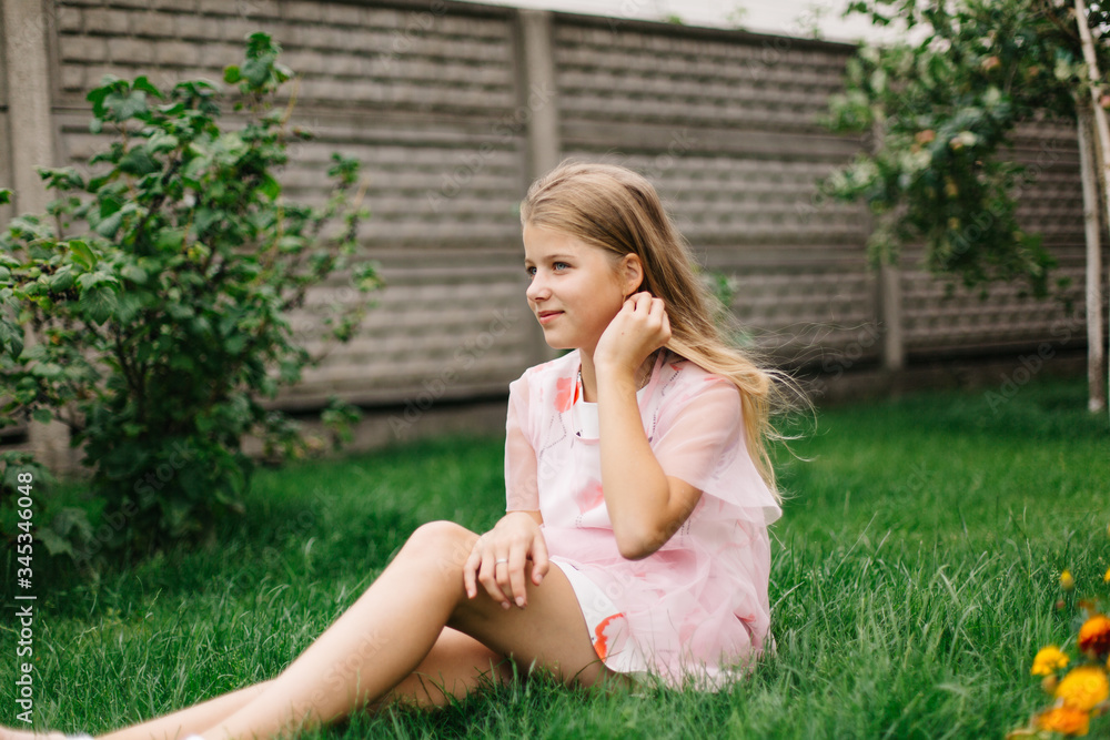 beautiful blue-eyed girl with long blond hair. little girl in a pink flamingo dress. summer bright, emotional photo. girl model with long hair sits on green grass beautiful blue-eyed girl with long blond hair. little girl in a pink flamingo dress. summer bright, emotional photo. girl model with long hair sits on green grass