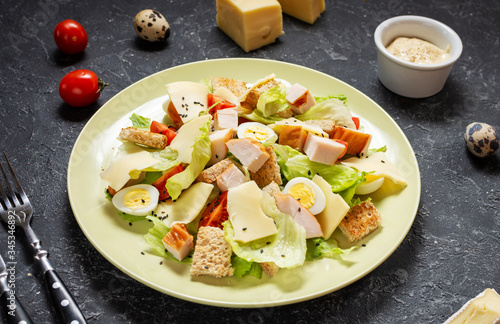 Fresh Caesar salad with delicious chicken breast, ruccola, spinach, croutons, egg, parmesan and cherry tomato on black stone background.