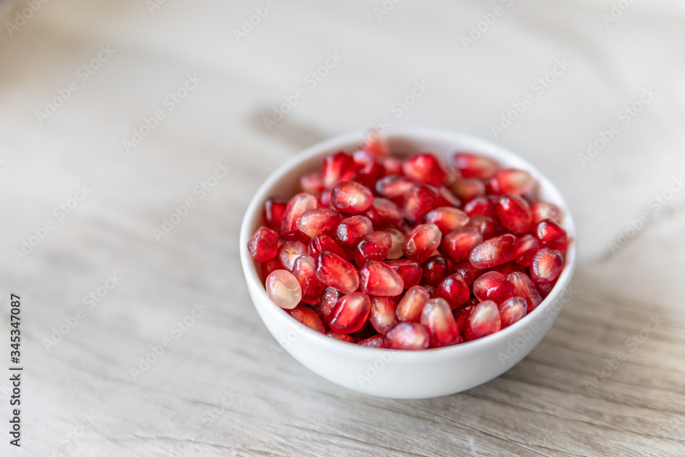 Pomegranate seeds in a small white bowl on a beige background Pomegranate seeds in a small white bowl on a beige background