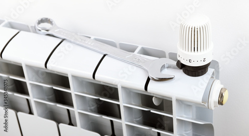 A wrench lies next to a thermostat on a heating battery in an apartment, office. Repair the radiator battery in the room. Repair and maintenance work, repair in the apartment. Heating recovery.