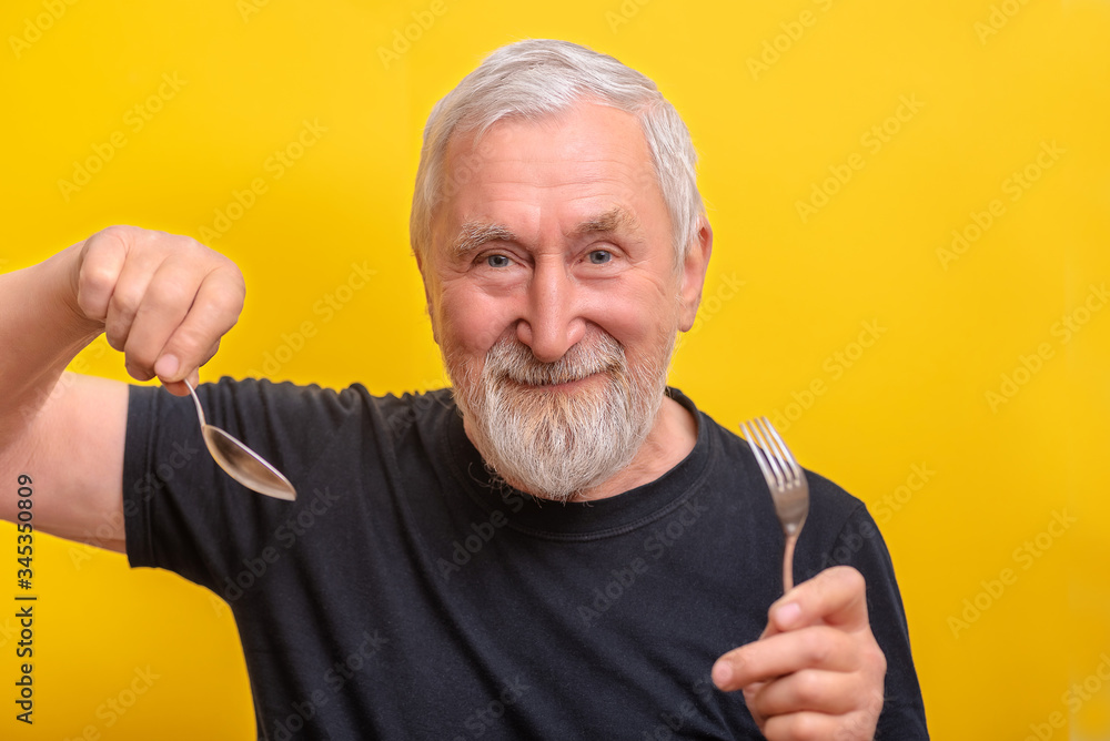 Senior man holds spoon and fork and over yellow background with copy space. Senior man take morning Senior man holds spoon and fork and over yellow background with copy space. Senior man take morning