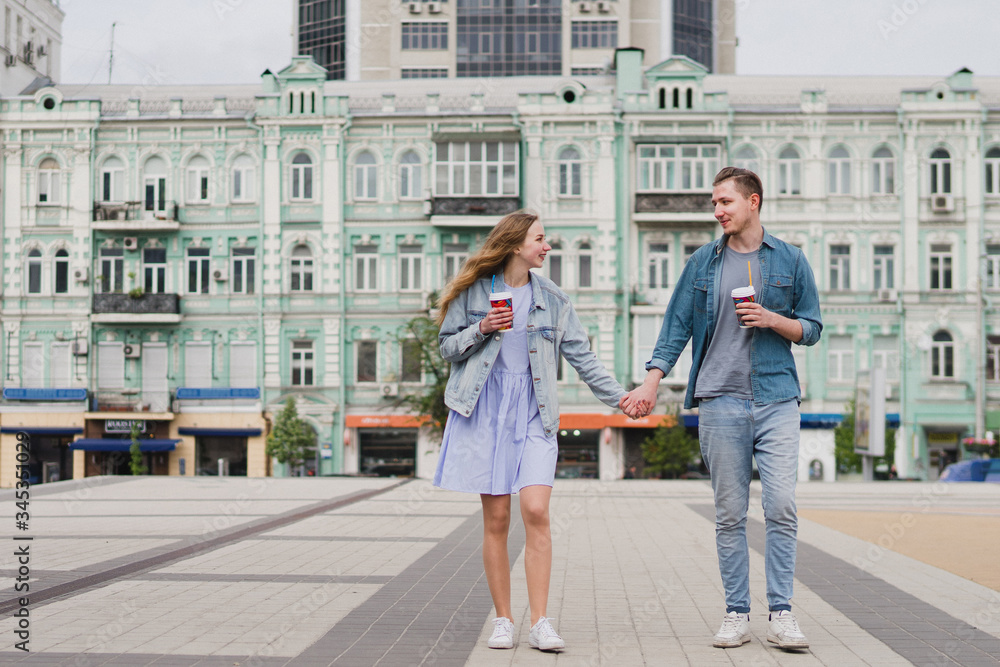 Romantic and happy caucasian couple in casual clothes walking together through the streets. Love, relationships, romance, happiness concept. Man and woman with disposable cups of coffee in the city.