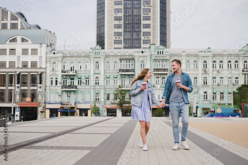 Romantic and happy caucasian couple in casual clothes walking together through the streets. Love, relationships, romance, happiness concept. Man and woman with disposable cups of coffee in the city. © anna_gorbenko