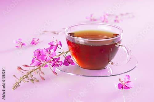 Cup with willow-herb tea and fresh flowers on pink background