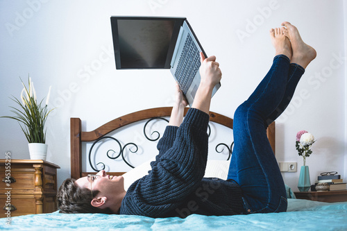 Woman lying on her back on a bed with her feet up and the laptop in her hands teleworking
 photo