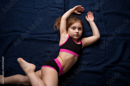 A white-skinned girl lies on a blue background in a beautiful pose. Sports girl. Childhood. Sport. Close-up.