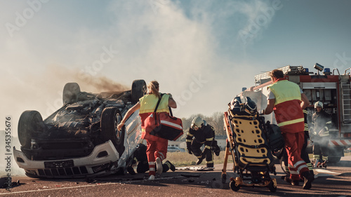 On the Car Crash Traffic Accident Scene: Paramedics and Firefighters Rescue Injured Victims Trapped in the Vehicle. Medics Use Stretchers, Perform First Aid. Firemen Grab Equipment.