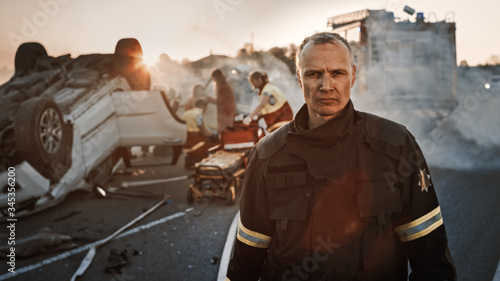 Portrait of the Brave Firefighter Walking to the Camera. In Background Courageous Heroes Paramedics and Firemen Rescue Team Fight Fire, Smoke and Save People’s Lives