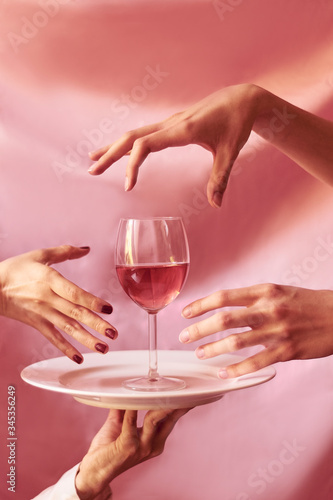 Many hands reaching a glass of wine.